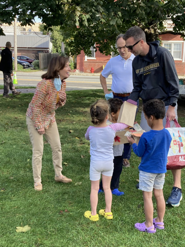 Three siblings eagerly showing off their scarecrow puppets to Governor Hochul at the Saranac Lake Farmers’ Market.