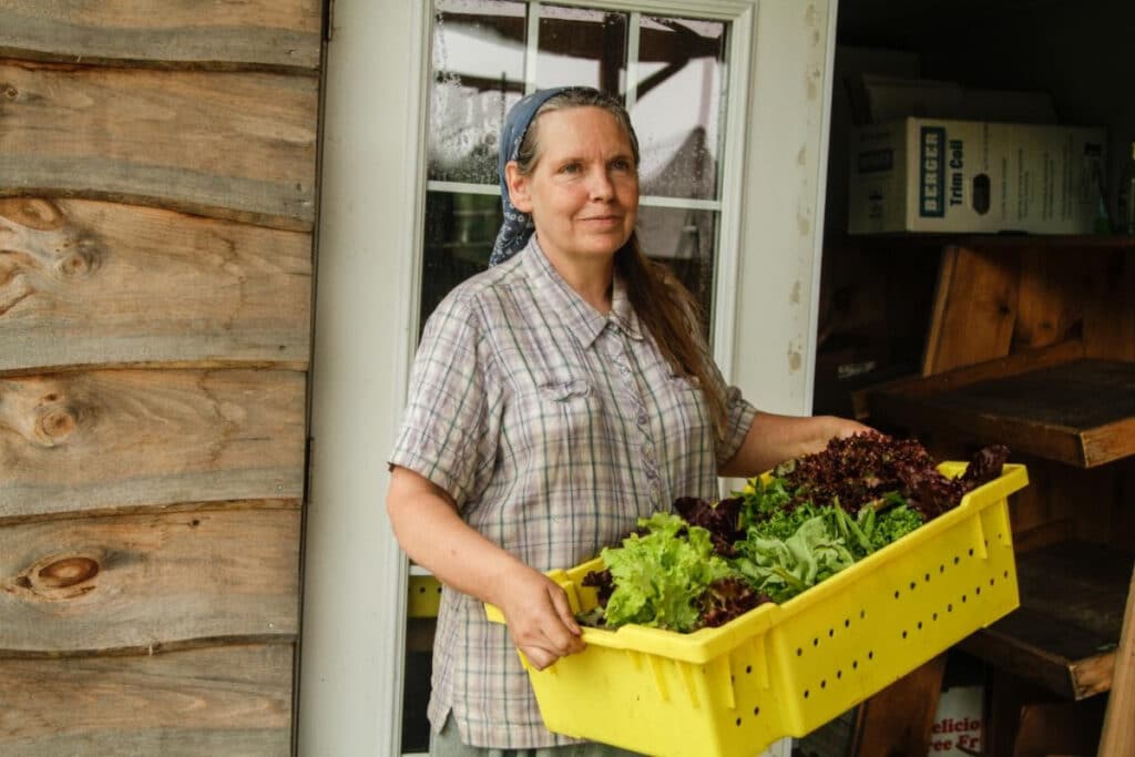 Photo depicts Cherie Whitten holding a yellow crate of fresh vegetables.