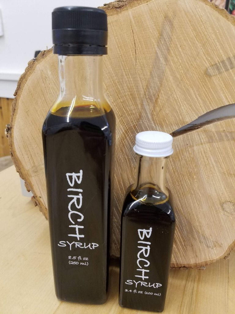 Thin, tall bottles of dark syrup. The bottle is labeled as Birch Syrup. 