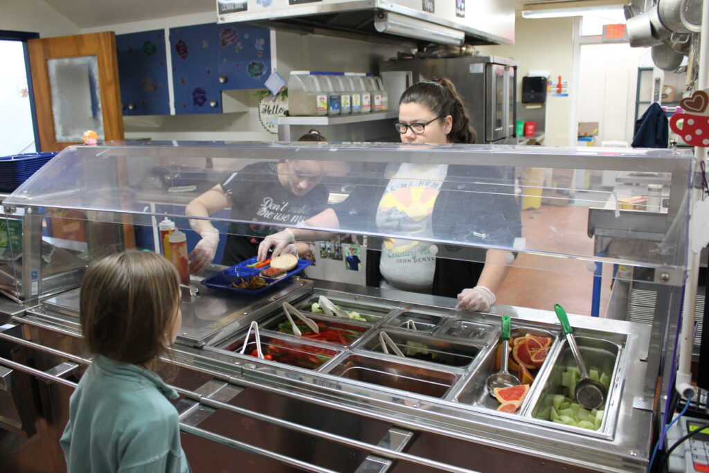Cafeteria workers serving food to a student