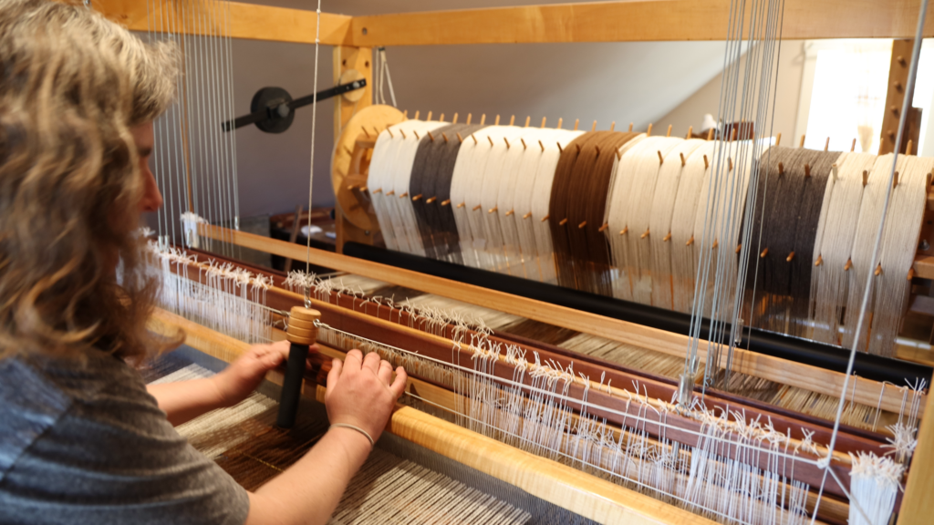Person weaving on a large wooden loom