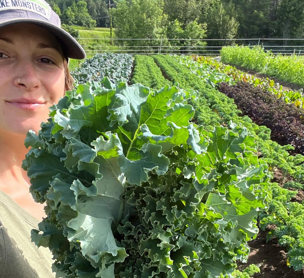 Person holding large green kale leaf in a garden