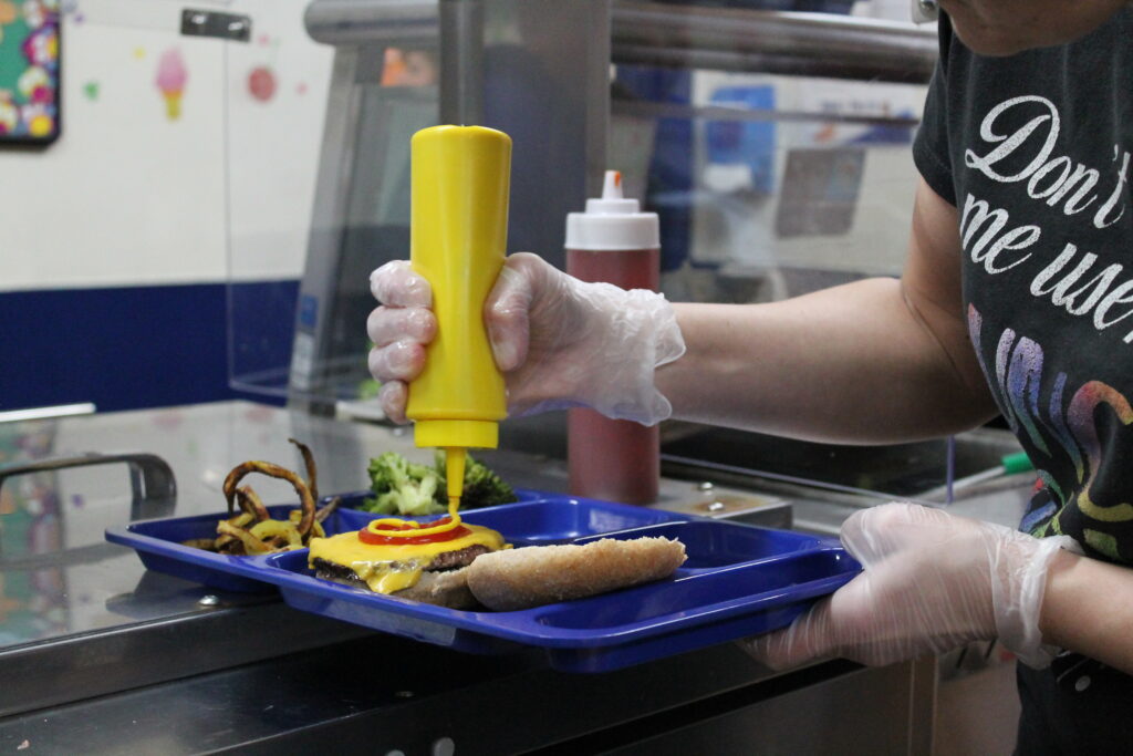 Person adding mustard to a hamburger on a tray