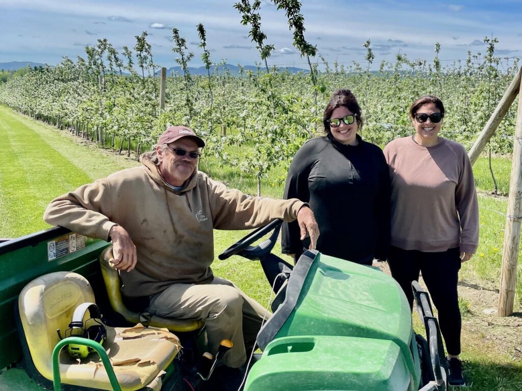 Three people posing on a tractor in an orchard