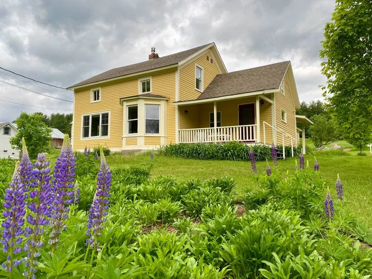 Yellow house with purple flowers and cloudy sky