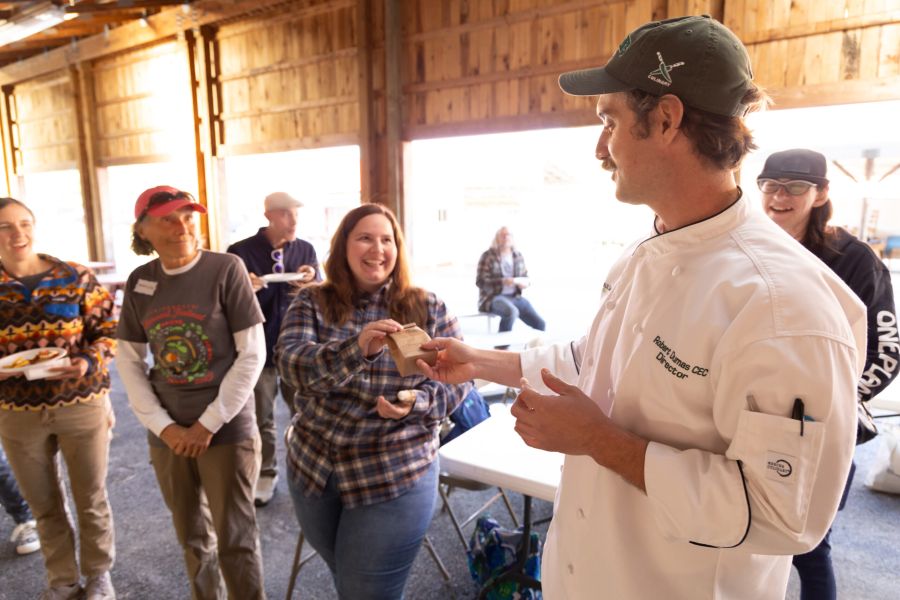 Chef handing a food sample to a smiling woman in a barn
